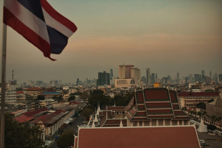 Bandera de Tailandia ondeando sobre los tejados de una ciudad tailandesa al atardecer