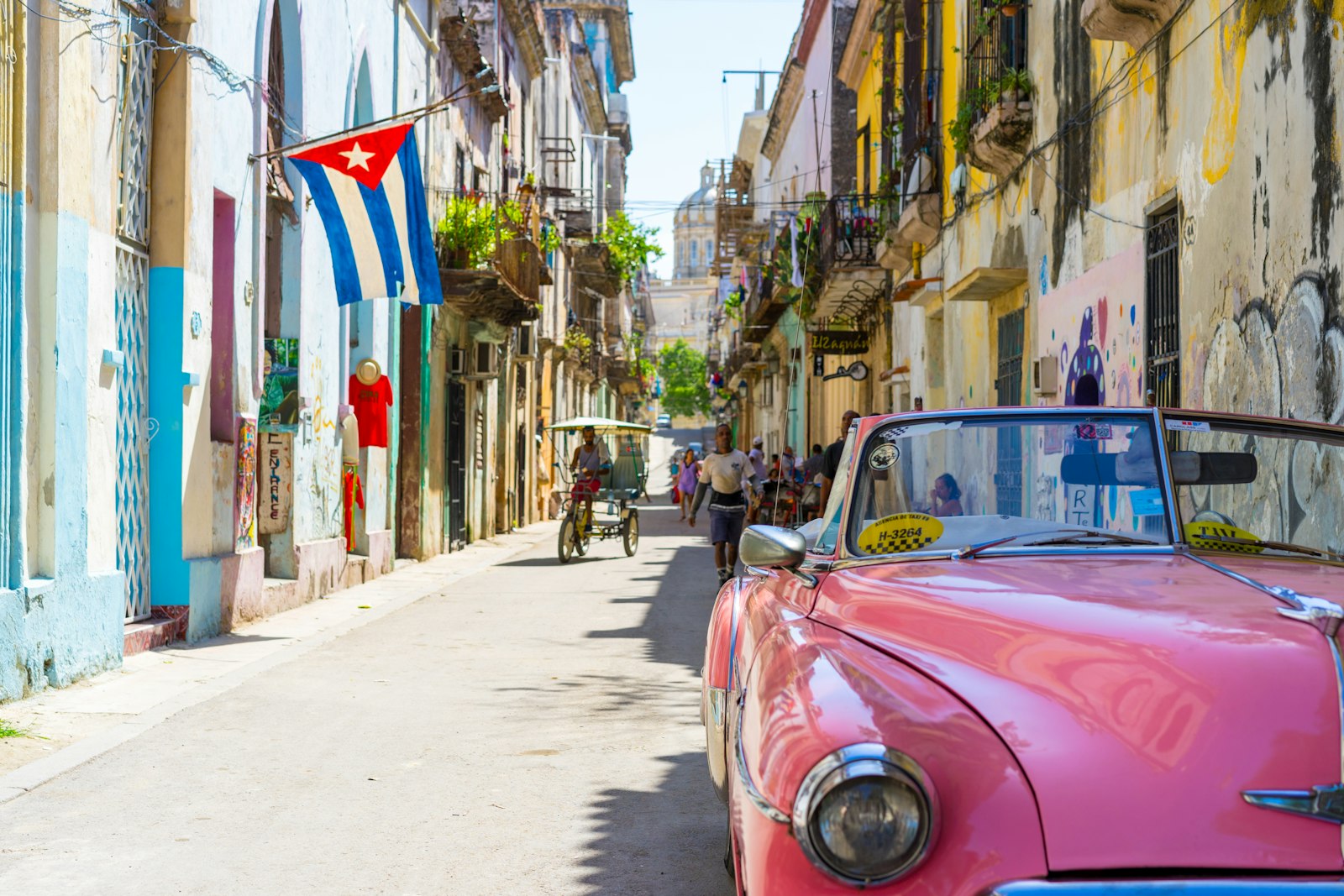 Calle de La Habana con un coche clásico rosa y una bandera cubana