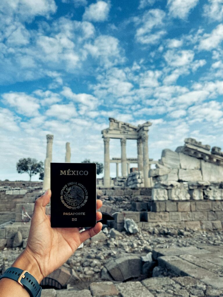 Viajero sosteniendo un pasaporte mexicano frente a unas ruinas antiguas