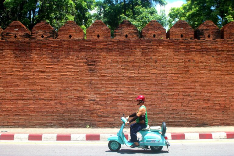 Motorista con casco en una scooter junto a una antigua muralla de ladrillo
